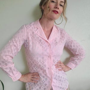 May include: A light pink button-down shirt with a geometric pattern. The long-sleeved blouse has a collared neckline and buttoned cuffs. The shirt is made of a sheer fabric.