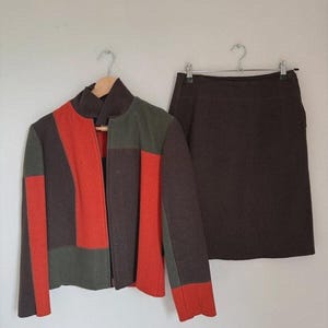 Peut inclure: Un ensemble deux pièces composé d'une veste et d'une jupe. La veste présente un design color-block en marron foncé, vert olive et orange vif avec un col montant et une fermeture éclair. La jupe assortie est d'une couleur marron foncé unie.