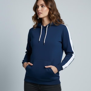 Puede incluir: Una sudadera con capucha azul marino con una franja blanca en las mangas y un bolsillo delantero. La sudadera con capucha tiene una capucha con cordón y está hecha de un material suave. El modelo lleva vaqueros negros.