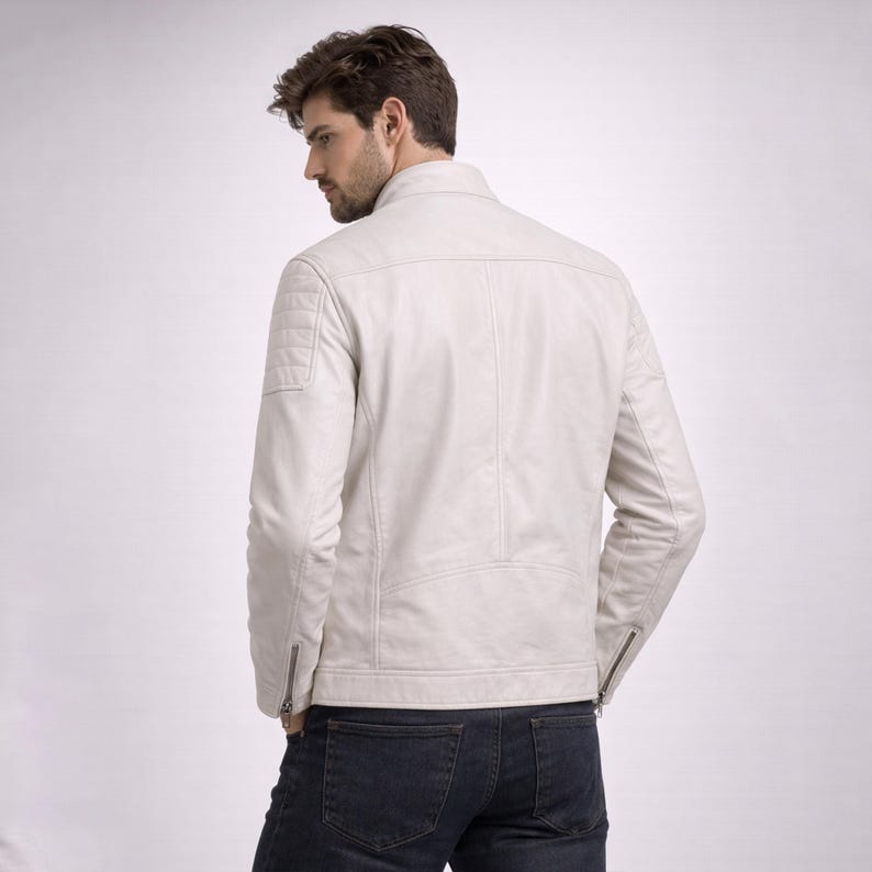 May include: A cream leather jacket with a stand-up collar and quilted shoulder detailing. The jacket features zip closures on the sleeves and a tailored fit. The model is wearing dark blue jeans.
