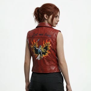 May include: A sleeveless red leather vest featuring a collar and a back graphic of a blonde figure holding a spear amidst stylized orange and yellow flames. The text Let me live is printed in black cursive script above the central illustration.