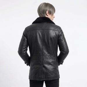 Puede incluir: Chaqueta de cuero negro con cuello de piel sint&eacute;tica negra. La chaqueta tiene cierre de botones y dos bolsillos delanteros. La persona lleva pantalones negros. La chaqueta es de estilo cl&aacute;sico.