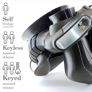 Op de afbeelding: Een zwart, gevormd plastic apparaat met een metalen vergrendelingsmechanisme met een sleutelgat. De tekst links luidt: Self bondage compatible, Keyless assisted release en Keyed assisted release, vergezeld van iconen van één persoon, twee personen en twee personen met een sleutel.
