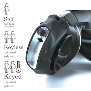 May include: A black device with a silver accent, featuring a keyhole design and the words "Self bondage compatible", "Keyless assisted release", and "Keyed assisted release". The device has a curved shape and a smooth, glossy finish.