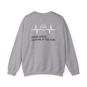 Op de afbeelding: Een lichtgrijs sweatshirt met witte tekst en een afbeelding van een hartslag met een stralingssymbool. De tekst luidt: "STEMI SPEED. CATH ME IF YOU CAN!". Dit is een kledingstuk met een medisch thema.