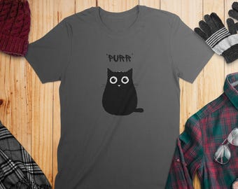 May include: A charcoal gray short-sleeved t-shirt featuring a centered graphic of a round black cat with large white eyes and the text 'PURR' printed in a black, stylized font above the cat's head. The shirt has a crew neckline.