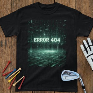 May include: Black t-shirt with a digital graphic in shades of green and the text "ERROR 404". The shirt is displayed with golf accessories, including tees and a golf club, on a wooden surface.