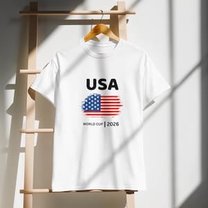 2026 USA World Cup soccer shirt – unisex white tee featuring bold 'USA' text and stylized American flag graphic, perfect for match day and fan gatherings