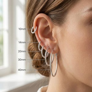 May include: A set of five silver hoop earrings of varying sizes, labeled with measurements from 10mm to 40mm. The earrings are thin, circular, and metallic, arranged in a vertical row along the earlobe and cartilage, showing the scale of each hoop.