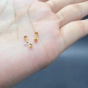 May include: Three gold-colored stud earrings. Two have a star shape, and one is a simple round stud. The earrings are small and delicate, suitable for various ear piercings. The earrings are displayed on a light skin tone.