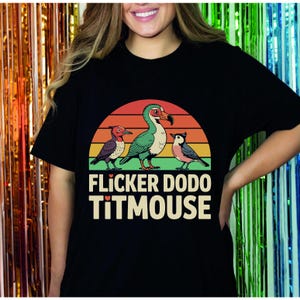Pode incluir: Uma camiseta preta com um gráfico de pôr do sol retrô com três pássaros. Os pássaros são um dodô, um chapim e um pica-pau. O texto "FLICKER DODO TITMOUSE" é impresso abaixo do gráfico.