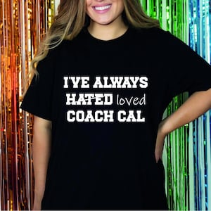 May include: Black t-shirt with white text that reads "I've always hated loved Coach Cal".