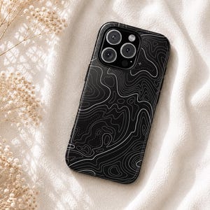 May include: A black smartphone case featuring a white topographic map line pattern across the entire back surface. The case has a rectangular camera cutout at the top left corner, revealing three circular camera lenses and a small flash component.