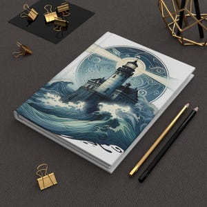 Op de afbeelding: Een wit notitieboek met een vuurtorenillustratie. De omslag toont een vuurtoren in een stormachtige zee, met een cirkelvormig ontwerp op de achtergrond. Gouden en zwarte potloden en gouden paperclips liggen op een donkergrijze ondergrond.