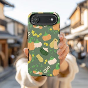 May include: A phone case featuring a repeating pattern of various pumpkins in shades of orange, green, and white, along with yellow star-shaped flowers and green vines, set against a muted green background. The case has a camera cutout.