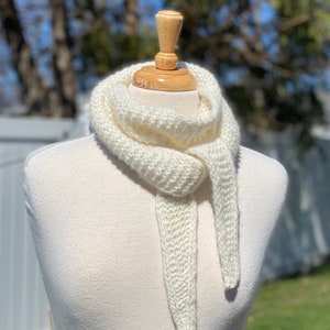 May include: A white knitted scarf with a simple design, displayed on a white mannequin.