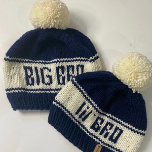 Puede incluir: Dos gorros de punto con pompones. El gorro m&aacute;s grande dice "Big Bro" en letras blancas sobre un fondo azul marino. El gorro m&aacute;s peque&ntilde;o dice "Lil Bro" en letras blancas sobre un fondo azul marino. Los gorros son azul marino y marfil.