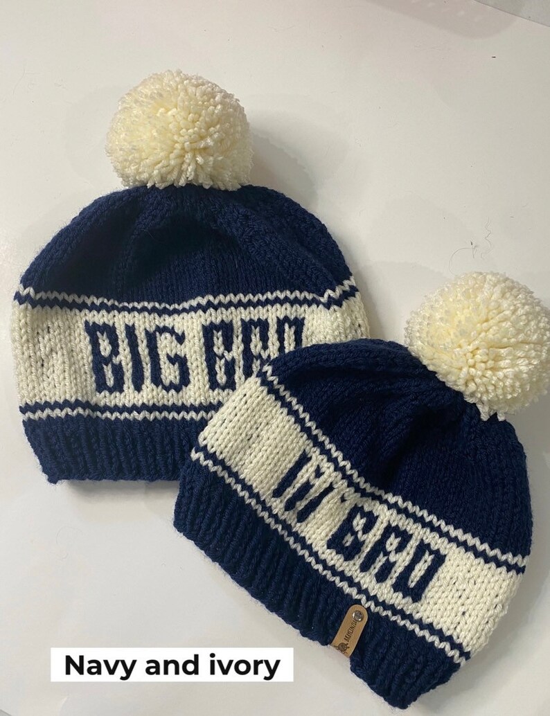 Puede incluir: Dos gorros de punto con pompones. El gorro m&aacute;s grande dice "Big Bro" en letras blancas sobre un fondo azul marino. El gorro m&aacute;s peque&ntilde;o dice "Lil Bro" en letras blancas sobre un fondo azul marino. Los gorros son azul marino y marfil.
