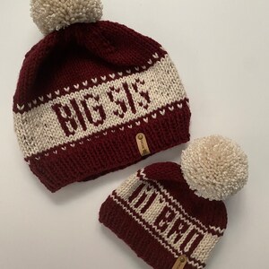 Puede incluir: Dos gorros de punto con pompones. El gorro m&aacute;s grande es burdeos con rayas blancas y el texto "Big Sis" bordado en &eacute;l. El gorro m&aacute;s peque&ntilde;o es burdeos con rayas blancas y el texto "Little" bordado en &eacute;l.