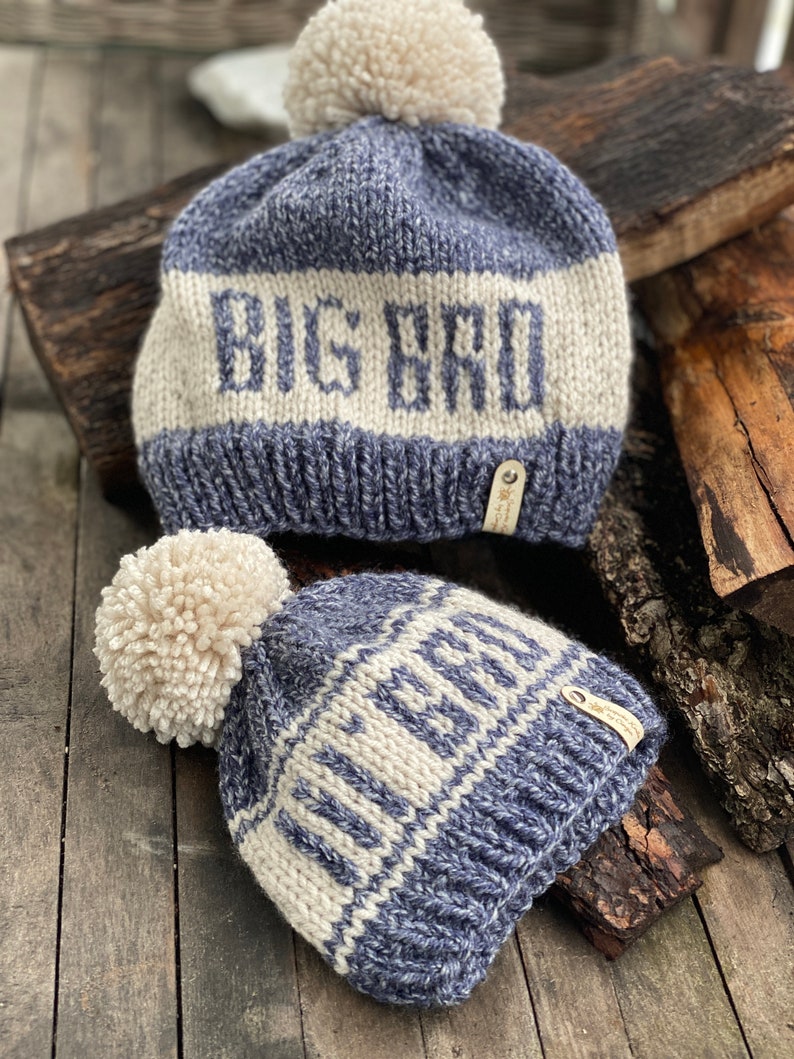 Puede incluir: Dos gorros de punto con pompones. El gorro m&aacute;s grande es azul y blanco con el texto "BIG BRO" en blanco. El gorro m&aacute;s peque&ntilde;o es azul y blanco con el texto "LITTLE BRO" en blanco.
