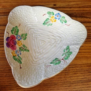 May include: A white ceramic triangular dish with a textured surface and a gold rim. The dish is decorated with a floral design in shades of red, pink, yellow, blue, and green.