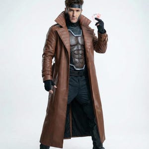 May include: A brown leather trench coat with a wide collar and a matching belt. The coat is worn over a black and brown chest piece and black pants. The person is holding playing cards and wearing black gloves and boots. A black headband completes the look.