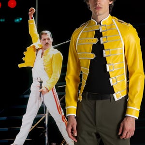 May include: A bright yellow jacket with silver accents and multiple buckles. The jacket is paired with black pants and a black shirt. A cutout of a person wearing a similar jacket and white pants is in the background.