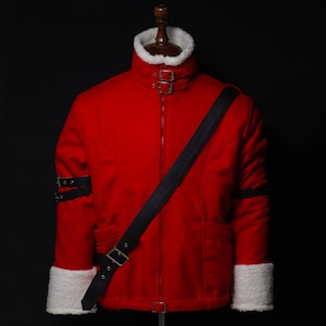 Puede incluir: Una chaqueta de color rojo brillante con cuello y puños de piel sintética blanca. La chaqueta incluye un cuello alto con dos hebillas plateadas, una correa negra diagonal en el pecho y dos correas con hebilla negra en cada manga.