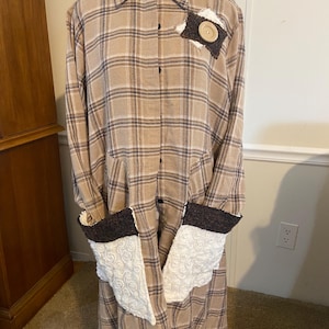May include: A long-sleeved plaid shirt with brown and white checks. The shirt has a button-up front and features white and brown fabric accents on the cuffs and pockets.