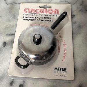 May include: A Circulon ringing saute timer in its original packaging. The timer is silver with a black handle and a dial that goes up to 30 minutes. The packaging includes the text "Kitchen Tools" and "It's functional."