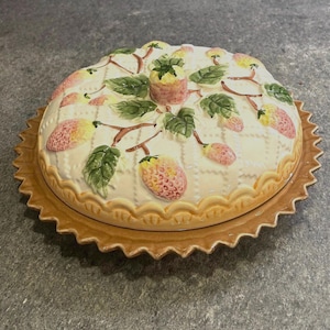 Könnte beinhalten: Eine Keramik-Kuchenform mit einem dekorativen Erdbeermuster. Die Kuchenform hat einen braunen, gewellten Boden und einen gewölbten Deckel. Der Deckel ist mit Erdbeeren, grünen Blättern und braunen Stielen verziert.