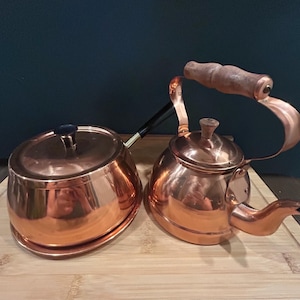 May include: A set of two copper kitchenware items. A copper pot with a lid and a copper teapot with a wooden handle.