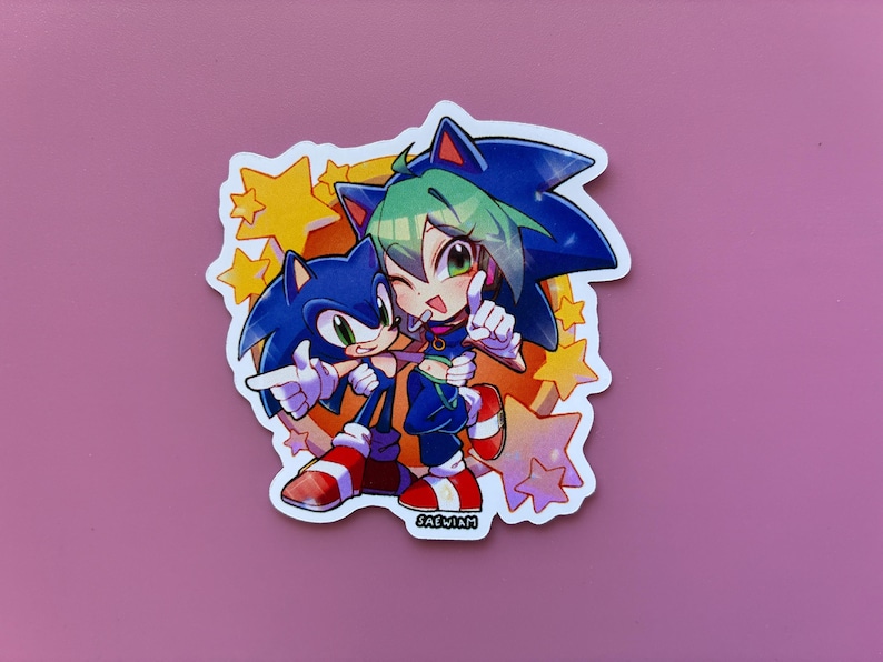 May include: A sticker featuring two cartoon characters, one resembling Sonic the Hedgehog, the other with green hair. They are hugging and pointing, surrounded by yellow stars. The sticker has a white border and the text "SAEWIM".