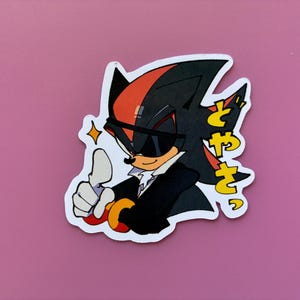 May include: A sticker featuring a cartoon character with black and red spiky hair, wearing sunglasses and a black suit. The character gives a thumbs-up gesture, with Japanese text to the right. A yellow star is next to the character.