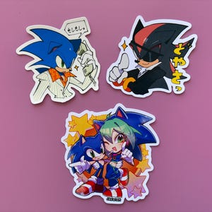May include: Set of three stickers featuring Sonic the Hedgehog and Shadow the Hedgehog in various poses. One sticker shows Sonic on the phone with Japanese text. Another shows Shadow giving a thumbs up. The third sticker shows Sonic with another character.
