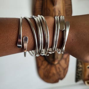 May include: A set of silver bangles stacked on a person's wrist. The bangles are thin and have a slightly curved shape.