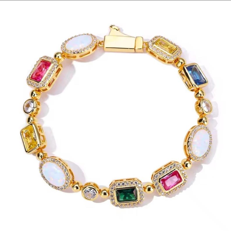 May include: Gold-toned bracelet featuring a variety of colorful gemstones. The bracelet includes oval, rectangular, and square-shaped stones in shades of pink, yellow, blue, green, and white. Each stone is set in a gold frame and accented with smaller, clear stones.