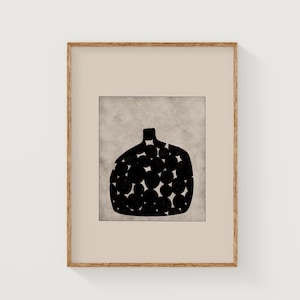 May include: An abstract art print showing a black vase-shaped design filled with circular patterns. The artwork is set against a textured, light grey background and framed in a natural wood frame. The style is minimalist and modern.
