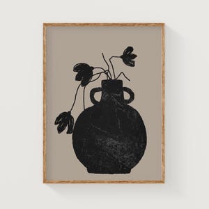 May include: A framed art print featuring a black vase with two handles, holding black floral stems against a tan background. The artwork has a minimalist, abstract style, with a wooden frame.