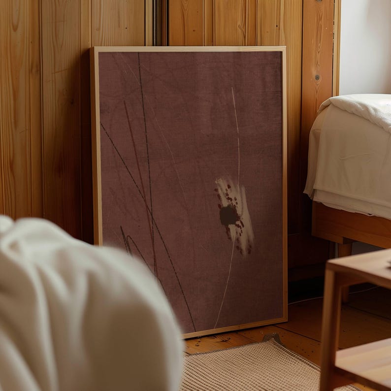 K&ouml;nnte beinhalten: Ein gerahmter abstrakter Kunstdruck mit einem ged&auml;mpften burgunderfarbenen Hintergrund und einem hellen Holzrahmen. Das Kunstwerk zeigt d&uuml;nne, dunkle Linien und eine wei&szlig;-braune, pinselstrichartige Form. Der Druck lehnt an einer Holzwand in einem Schlafzimmer.