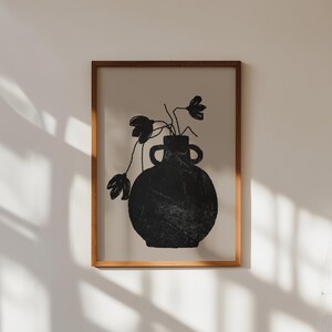 May include: A framed art print featuring a black vase with two handles, holding black floral stems. The artwork has a textured appearance and is set against a neutral background. The frame is made of wood.
