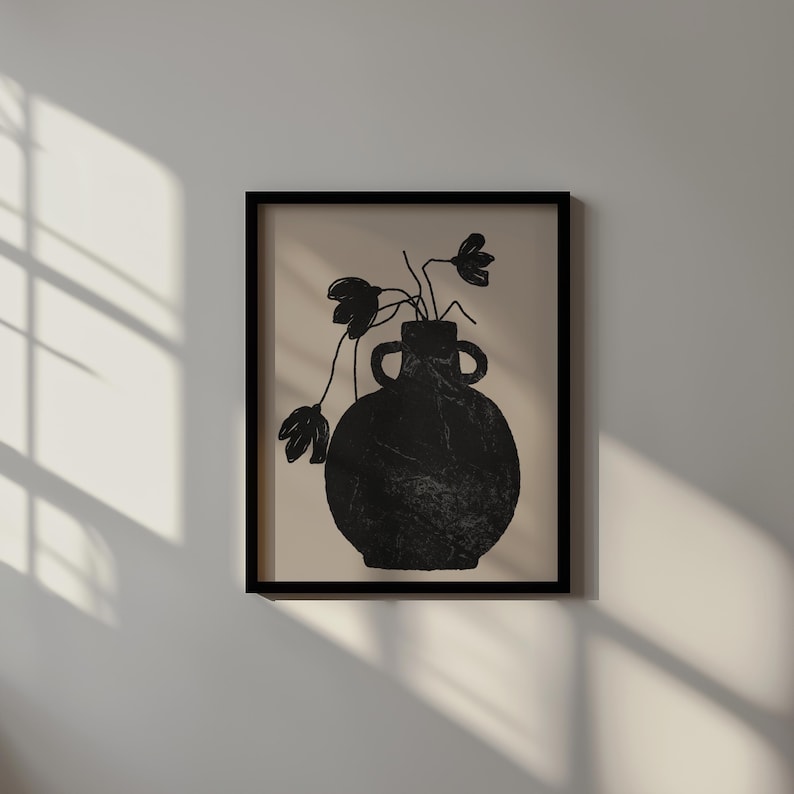 May include: Black framed art print featuring a black vase with two handles, holding black flowers against a beige background. The vase has a textured appearance. The artwork is displayed on a white wall with shadows.