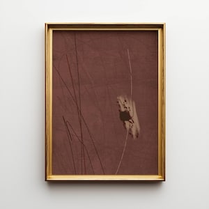 K&ouml;nnte beinhalten: Abstrakter Kunstdruck in einem goldenen Rahmen. Das Kunstwerk zeigt einen weinroten Hintergrund mit d&uuml;nnen, dunkelbraunen Linien und einer wei&szlig;en und braunen abstrakten Form. Der Rahmen hat eine einfache, rechteckige Form mit Goldfinish.