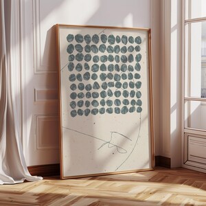 May include: A framed abstract art print with a beige background and a grid of blue circles. The print has a simple line drawing of a hat in the bottom right corner.