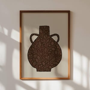 Puede incluir: Una impresión artística enmarcada que presenta un jarrón marrón con dos asas. El jarrón tiene un patrón floral detallado en un tono marrón más oscuro. La obra de arte está sobre un fondo crema y enmarcada en un marco de madera.
