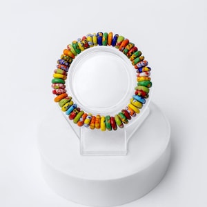 Puede incluir: Un brazalete de cuentas coloridas con una variedad de cuentas pequeñas y redondas en tonos de rojo, naranja, amarillo, verde, azul y morado. Las cuentas están dispuestas en espiral y enhebradas en un cordón elástico transparente.