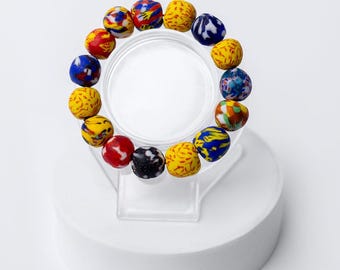 May include: A colorful bracelet made of round beads with intricate patterns in shades of blue, yellow, red, and white. The bracelet is displayed on a white pedestal.
