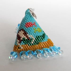 Peut inclure: Une petite décoration triangulaire bleue en perles avec un charme argenté. La décoration est ornée d'un motif de poissons, d'une maison et d'une scène de plage. La décoration est attachée à une chaîne de perles transparentes.