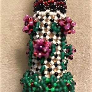 May include: A beaded flower design featuring pink, green and red beads. The beads are arranged in a pattern resembling a flower stem with leaves and flowers.