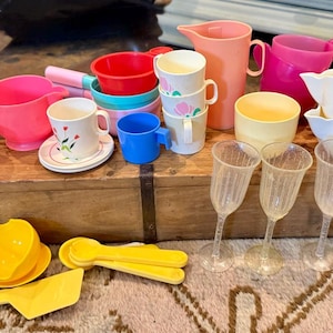May include: A collection of vintage children's play dishes and serving pieces in various colors. Includes pink, red, blue, and yellow cups, bowls, pitchers, and serving utensils. Also includes clear plastic goblets.